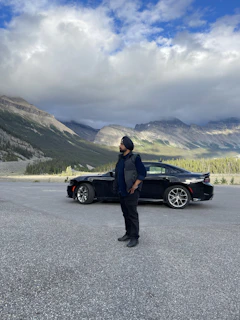 A friendly driver standing beside a clean, comfortable cab with mountain roads in the background.