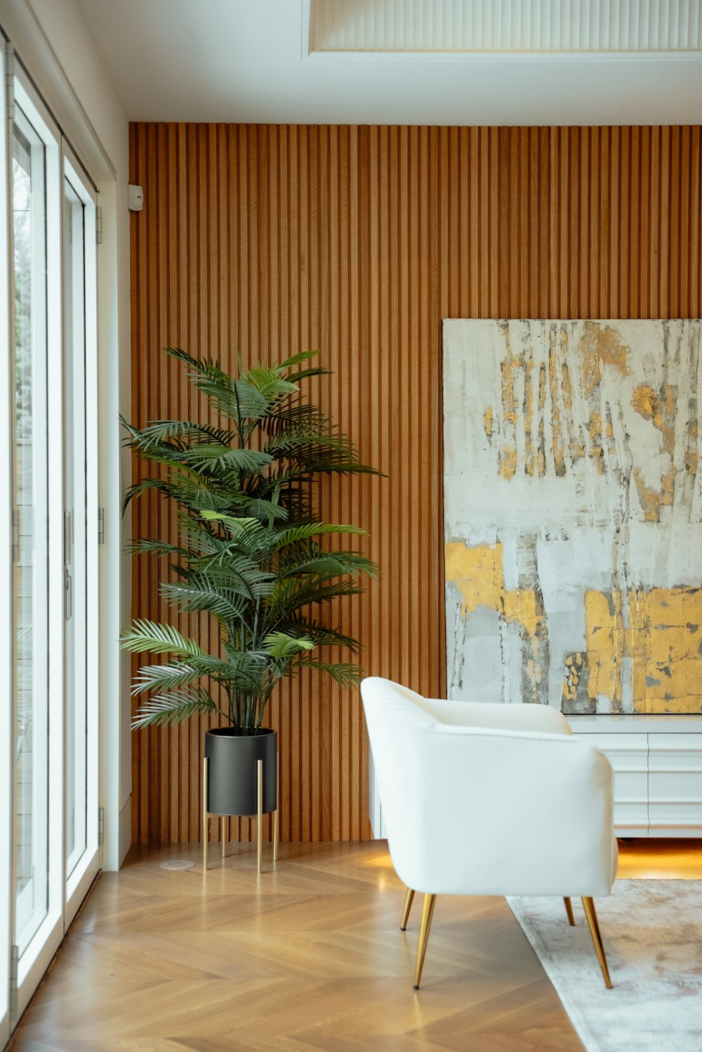 a chair and a plant in a room with a wall with a painting