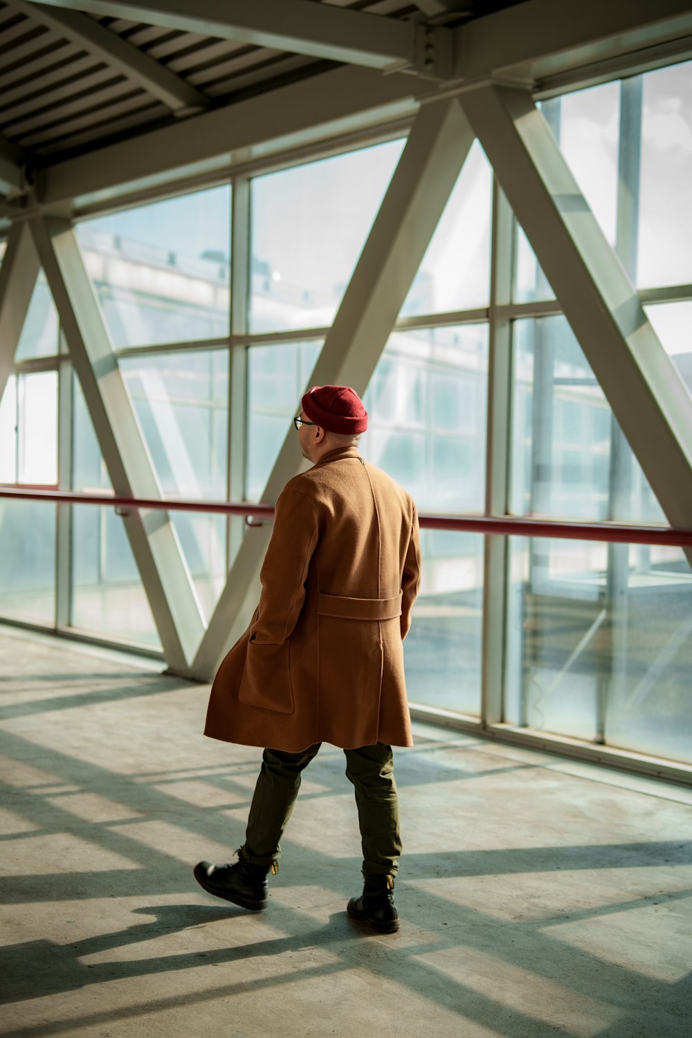 a person in a coat and hat standing in front of a large window