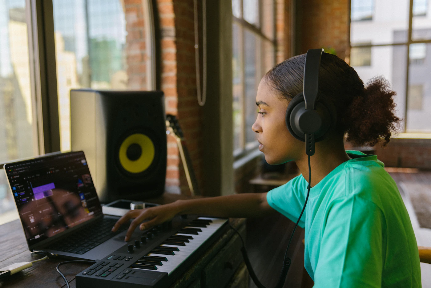 Musisi memakai headphone dan memainkan keyboard di depan laptop dalam studio rumahan