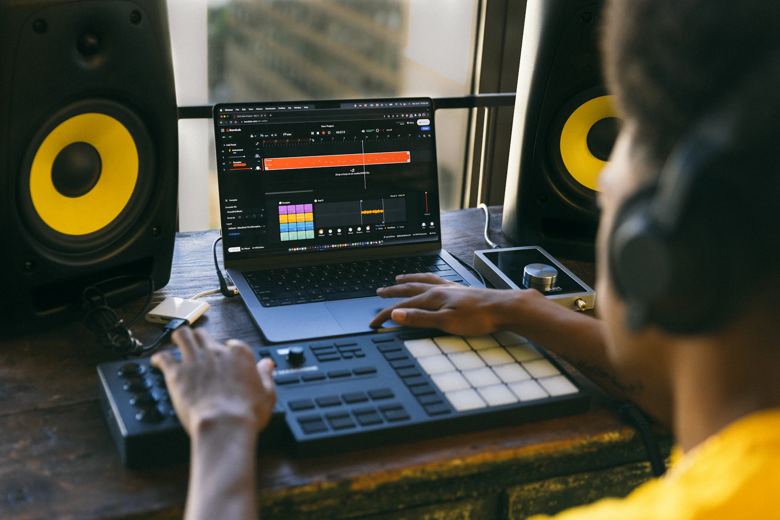 Producer creating music at a laptop and MIDI controller between studio monitors
