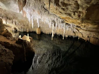 Stalactites hanging over calm, reflective water in the Chihuanche cave.