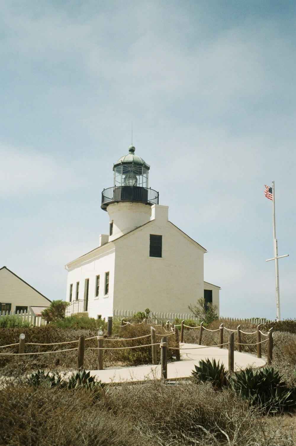 a white building with a flag on top with Old Point Loma Lighthouse in the background