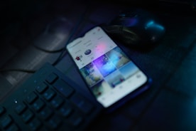 Hands typing on a smartphone with social media apps open, set against a dark workspace.