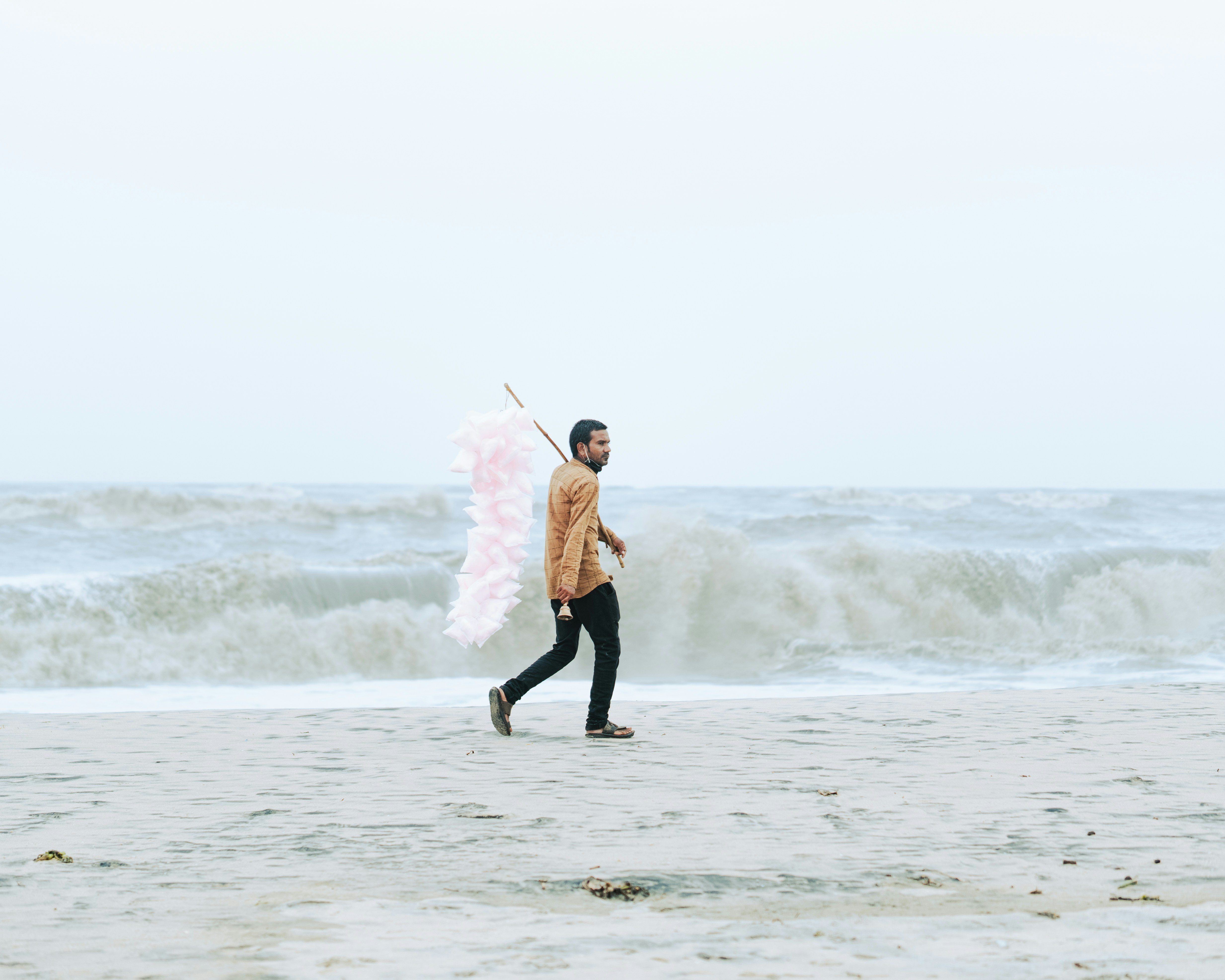 Man with large pink wings walks on a beach.
