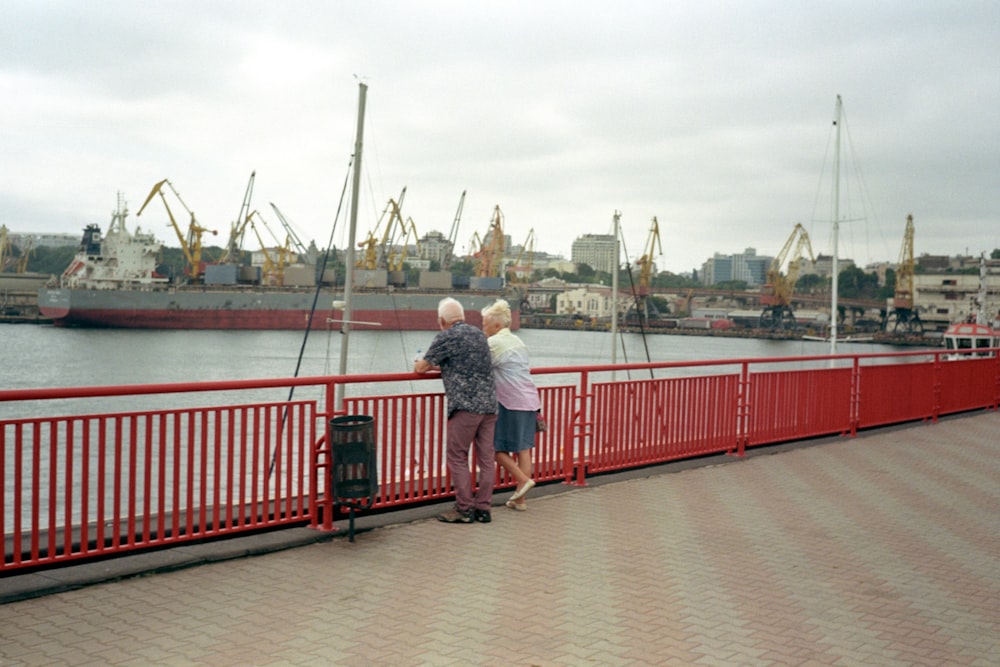 a couple of people standing on a bridge looking at a large ship