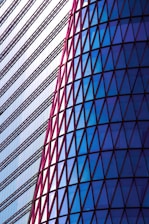 A striking architectural design featuring a modern building facade. The left side consists of horizontal lines with a minimalist style, while the right side displays a series of triangular glass panels in a spectrum of blues framed by red outlines.