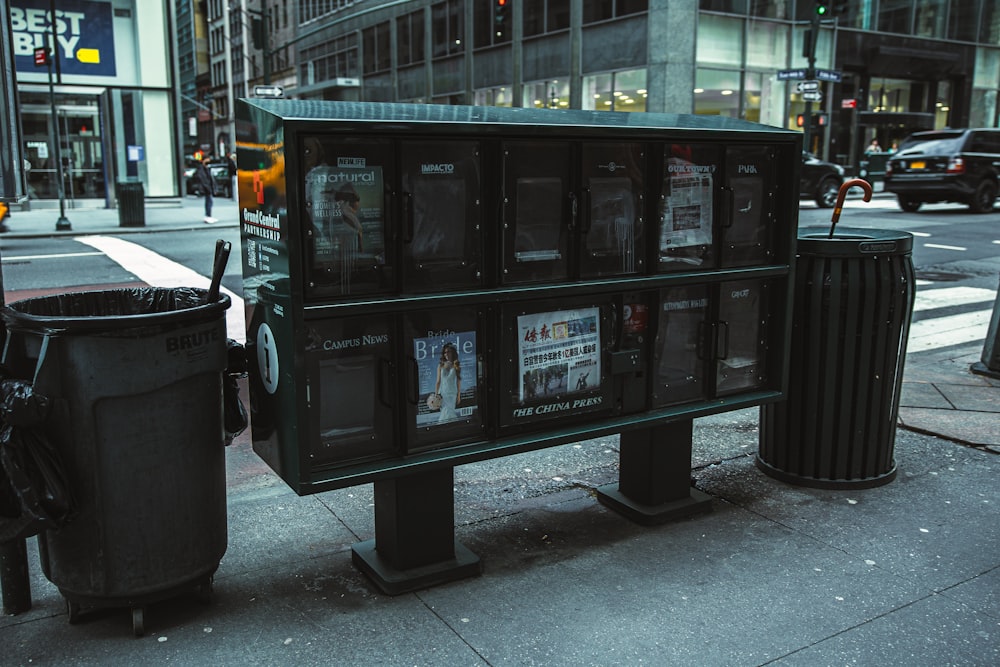 a black trash can next to a trash can on a sidewalk