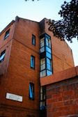 A brick building with multiple windows, featuring a sign that reads 'Leading to Weaver Street'. The architecture highlights a blend of traditional brickwork and modern glass elements. Trees and foliage partially frame the scene, adding a natural contrast.