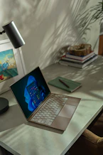 A cozy office desk with a laptop, a blue notebook, and a golden pen reflecting the brand colors.