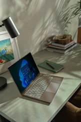A cozy office desk with a laptop, a blue notebook, and a golden pen reflecting the brand colors.