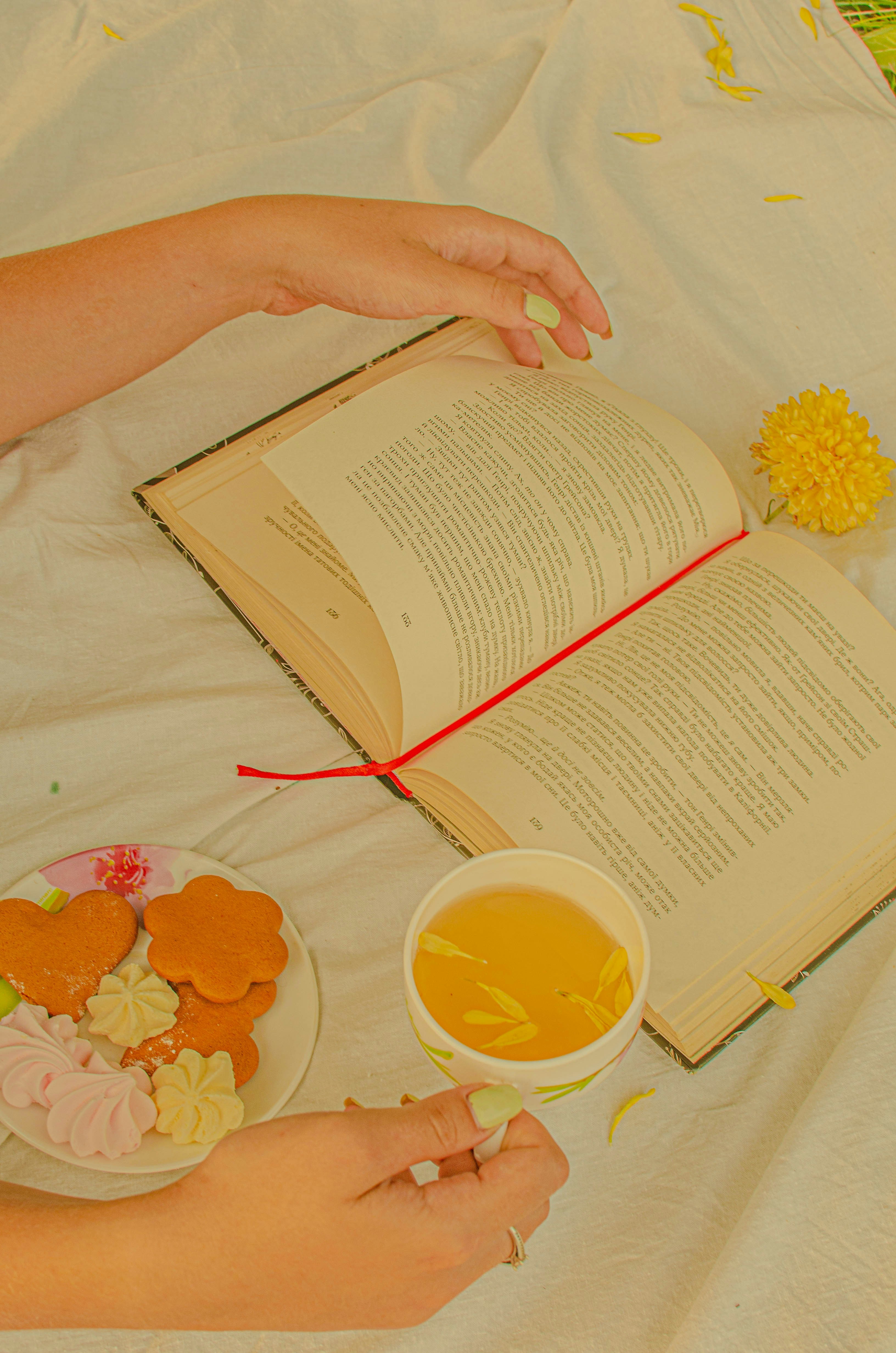 a person's hands holding a book and a cup of tea