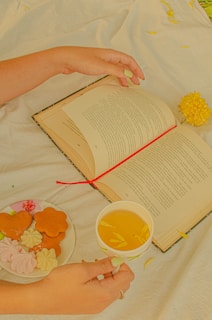 a person's hands holding a book and a cup of tea