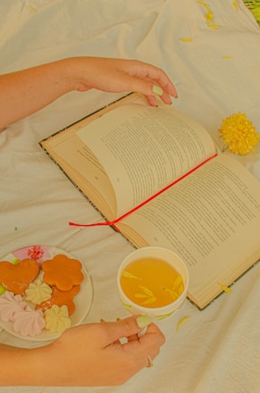 a person's hands holding a book and a cup of tea
