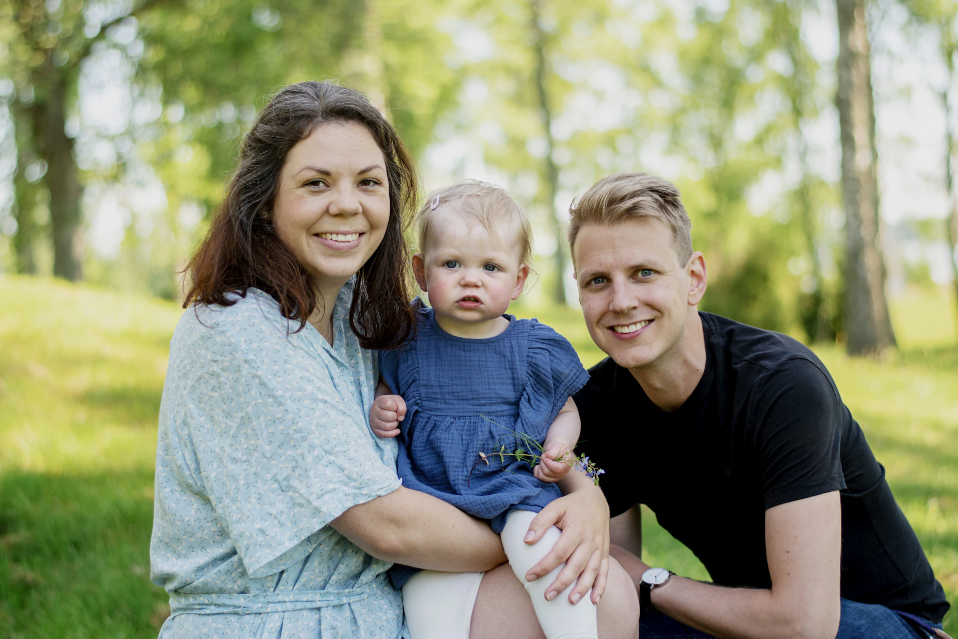 a man woman and child sitting on grass with trees in the background
