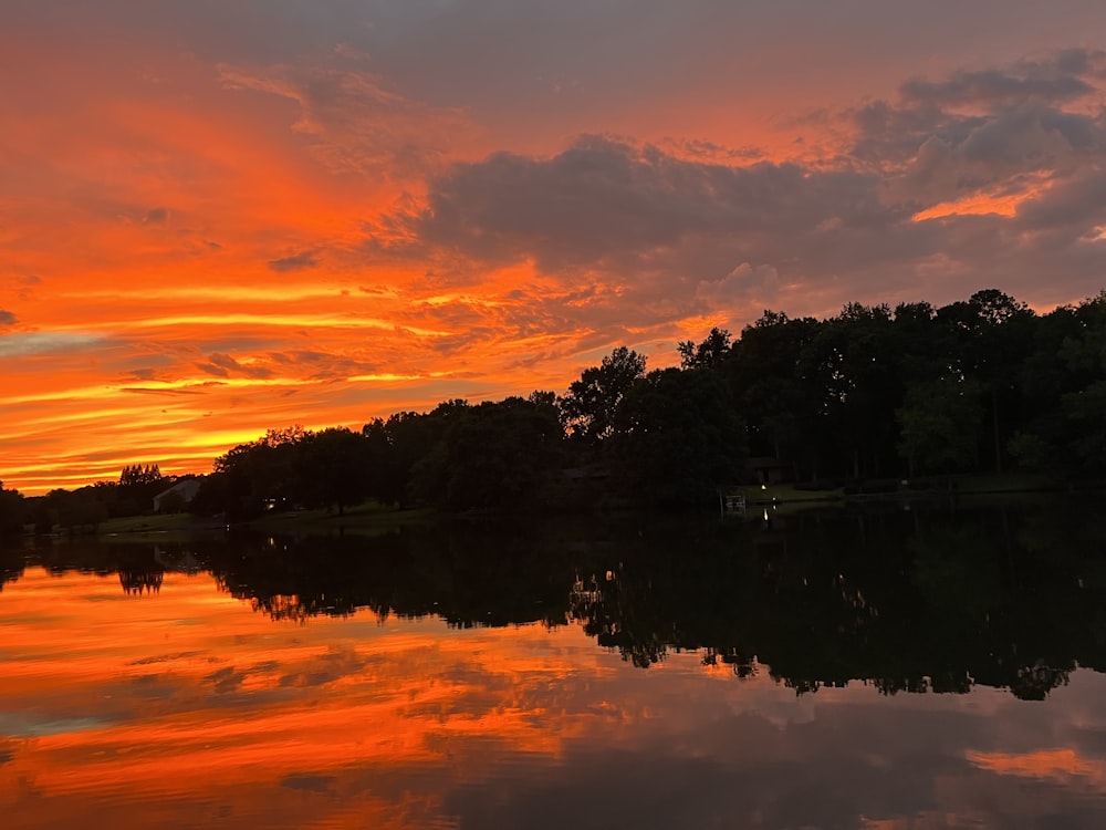 um corpo de água com árvores e um pôr do sol ao fundo