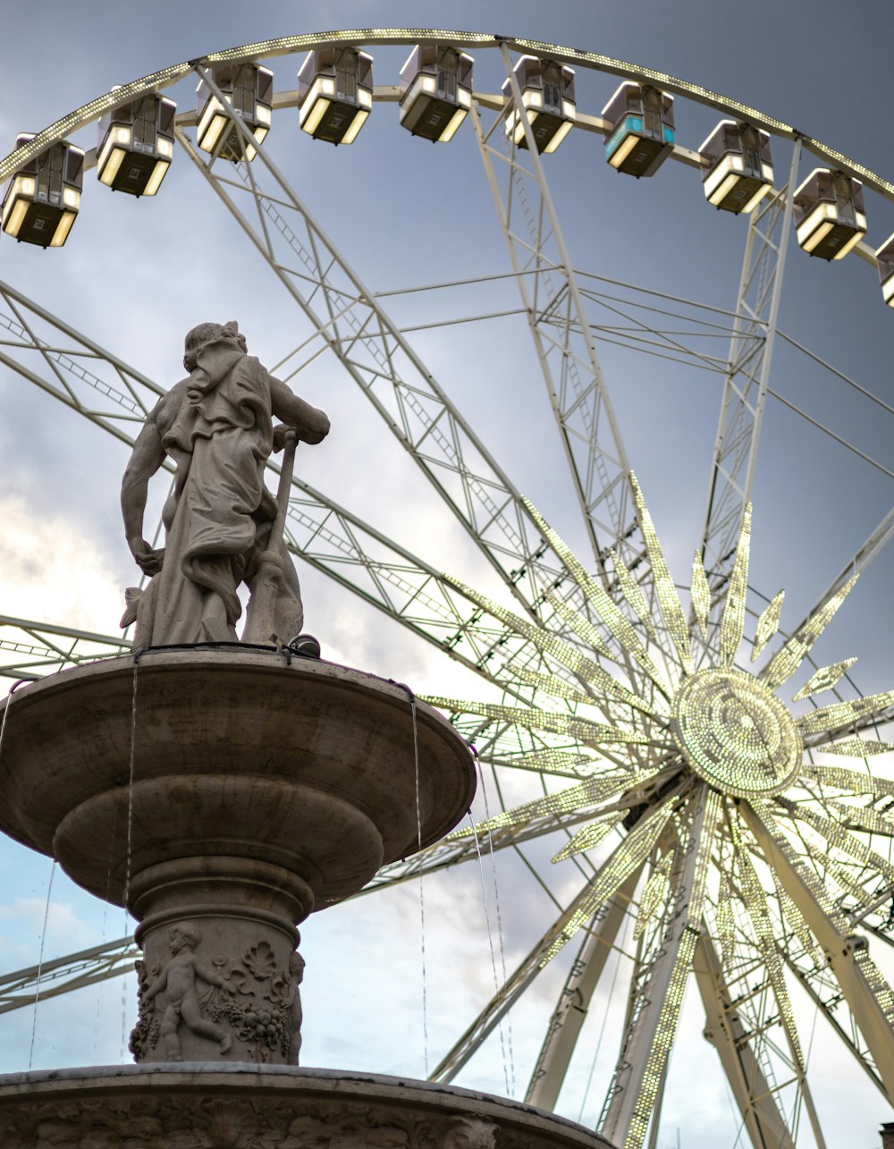 a statue of a person sitting on a fountain in front of a ferris wheel