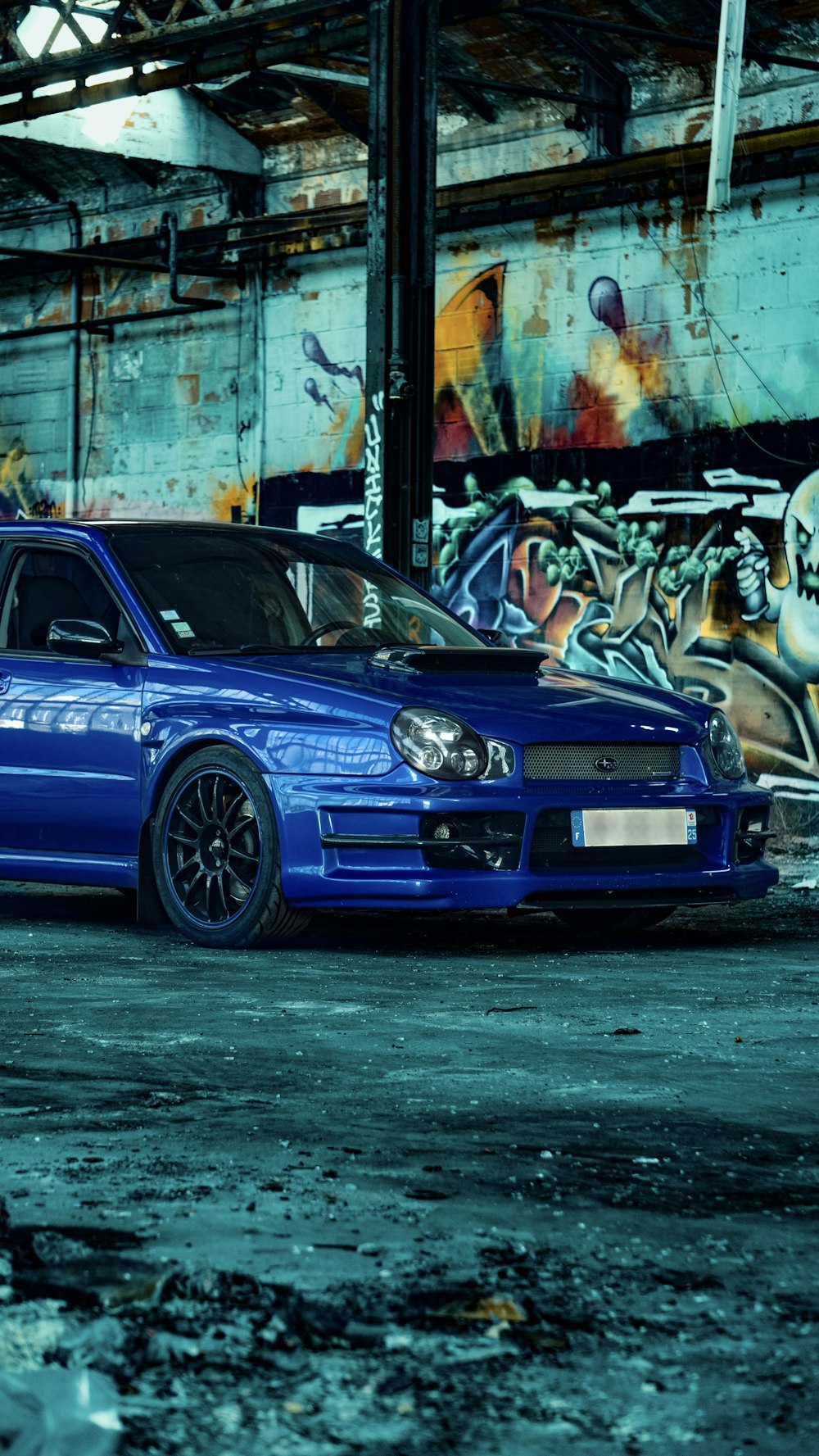 a blue car parked in front of a building with graffiti on it