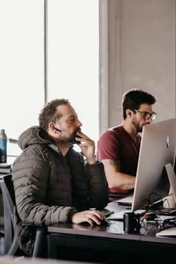 men sitting at a desk looking at a computer screen