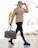 A person walks confidently, dressed in a beige leather jacket, black ripped jeans, and chunky black boots. They wear a leopard print hat and black gloves, accessorized with sunglasses and a gold chain necklace. The person carries a designer travel bag in one hand.