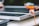 A close-up view of a measuring tape placed on the edge of a solar panel. The focus is on the transparent measuring tape with an orange strap, while the solar panel beneath has a metallic frame. The background is slightly out of focus, adding depth to the composition.