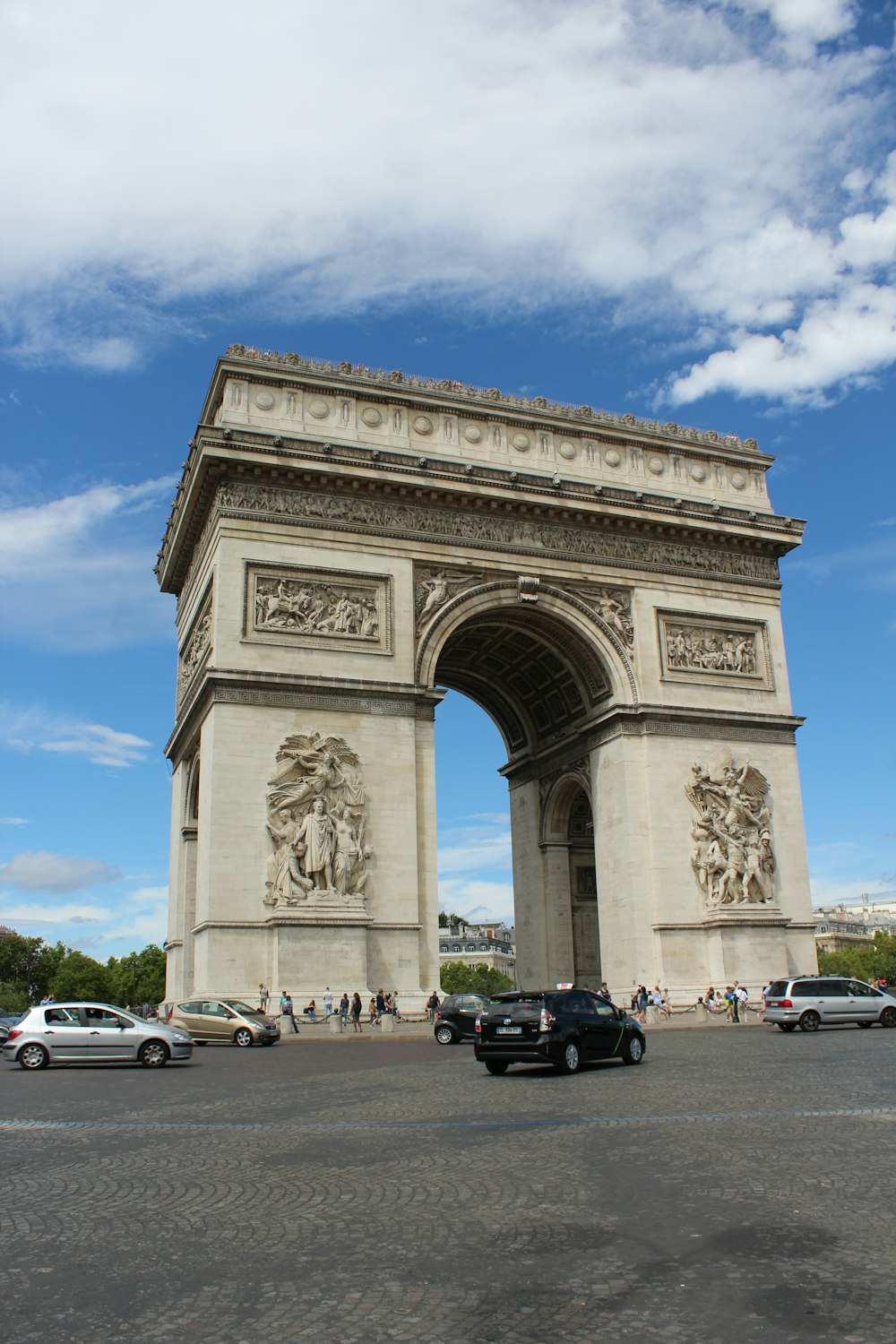 a large stone arch with statues with Arc de Triomphe in the background