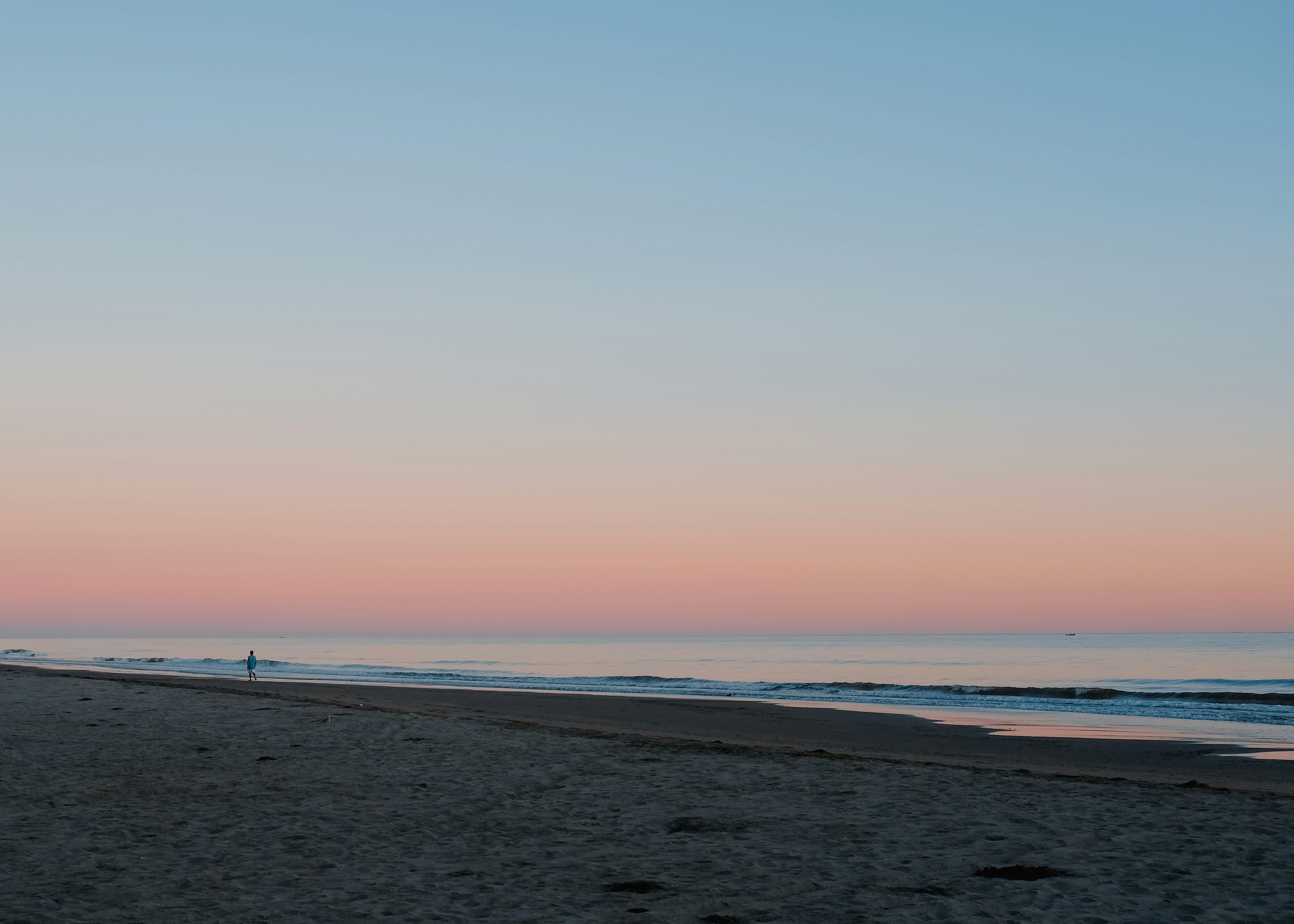 Marina Beach Chennai at sunrise with calm waves and soft pink sky with silhouettes of morning walkers