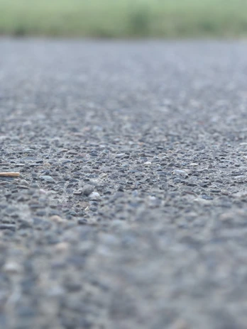 Close-up of a professional applying asphalt sealant on a driveway under bright daylight.