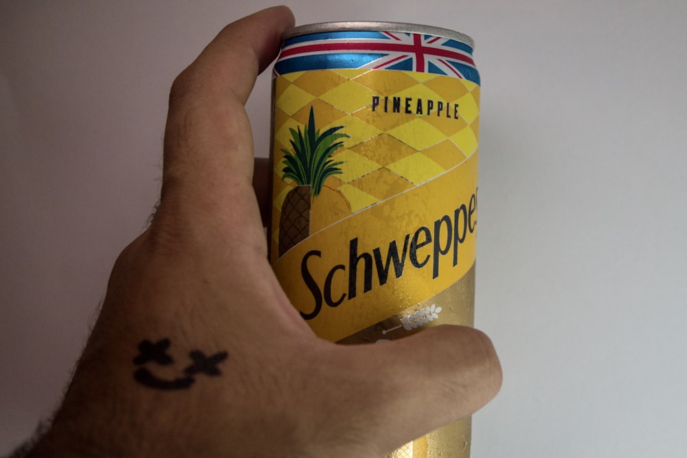 uma mão segurando uma lata amarela e vermelha com um logotipo preto e branco
