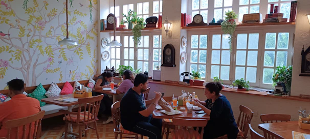 Cozy corner of the tinumatre café with wooden tables, potted plants, and customers enjoying their coffee and cakes.