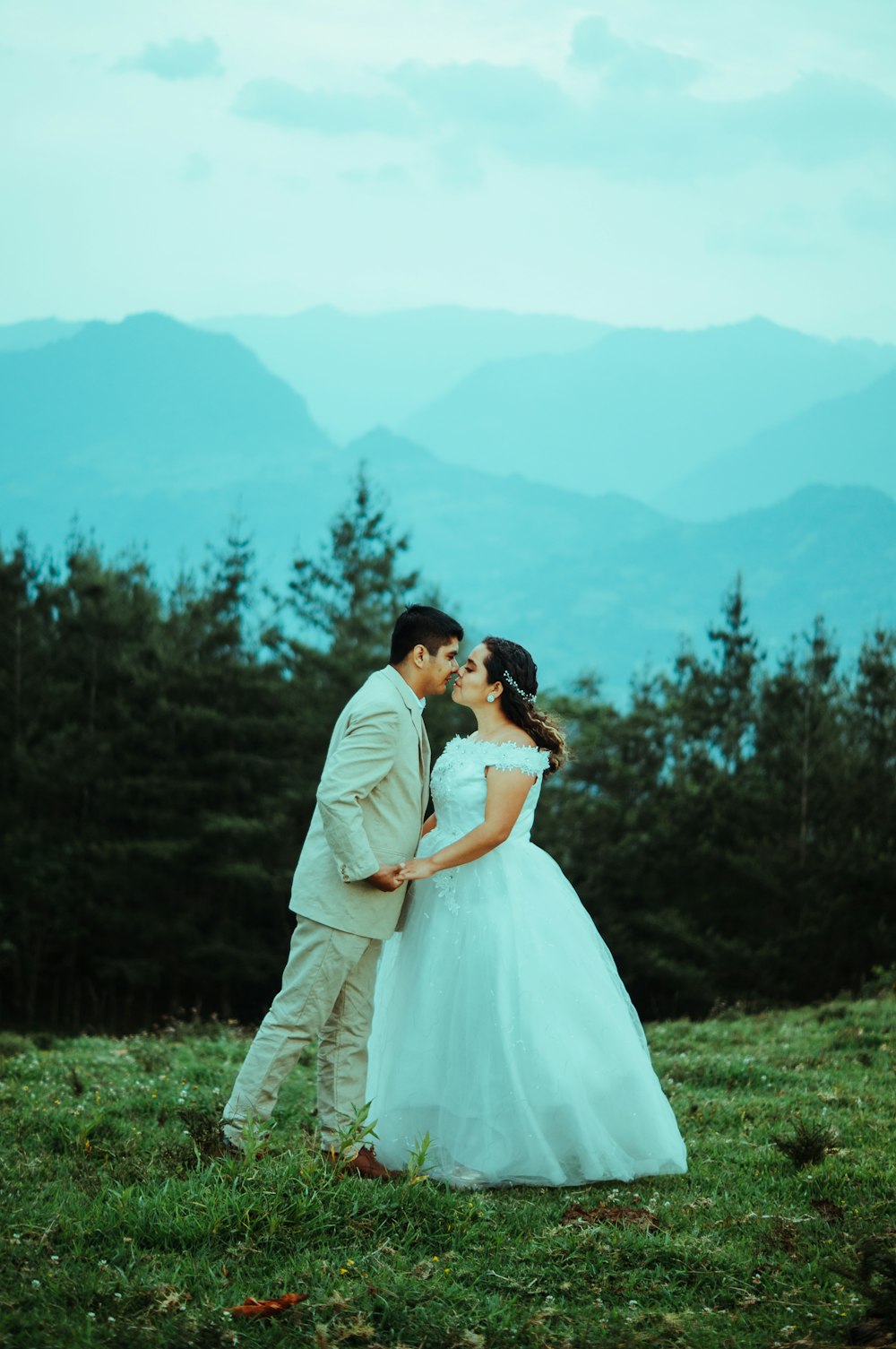 a man and woman kissing in a field with trees and mountains in the background