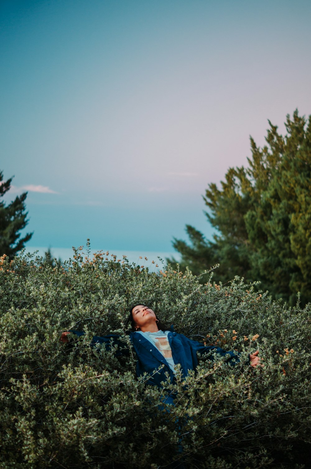 a man lying in a field of plants with water in the background