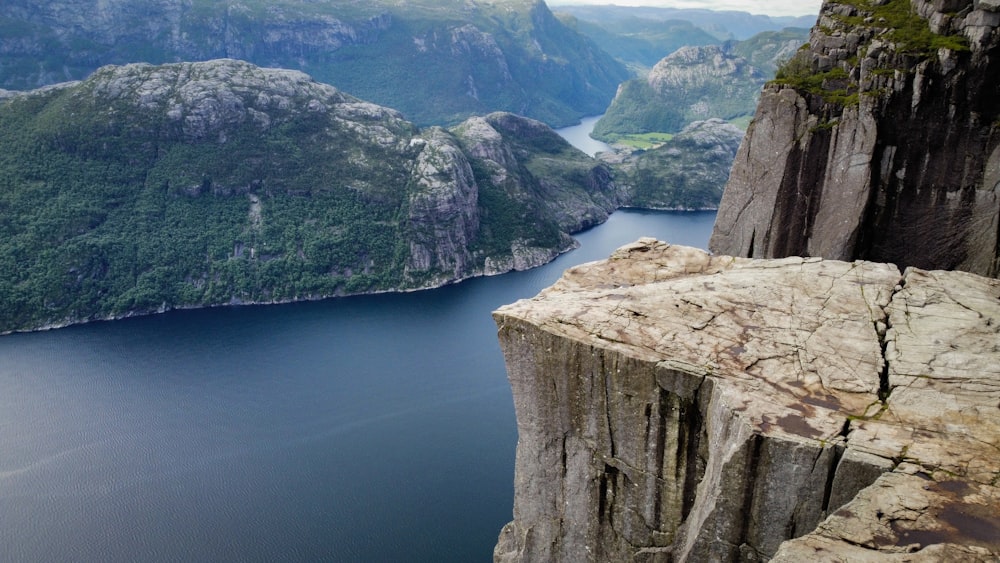 a cliff with a body of water below with Preikestolen in the background