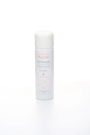 Close-up of Avène thermal water spray misting over a fresh face in a serene spa setting.