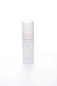 Close-up of Avène thermal water spray misting over a fresh face in a serene spa setting.