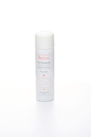 A white spray can with a rounded cap, featuring the brand Av&egrave;ne and labeled as Eau Thermale Thermal Spring Water. The packaging includes orange text and minimalistic design elements. It appears to be a product aimed at providing soothing and anti-irritating benefits for sensitive skin.