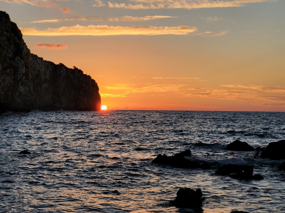 a body of water with rocks and a sunset