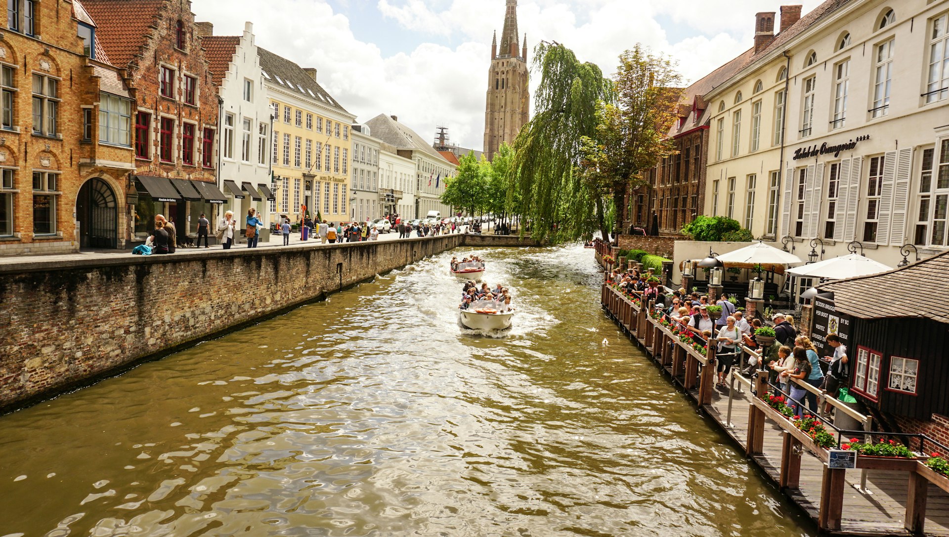 A canal boat gliding past classic Bruges townhouses with the Church of Our Lady's spire in the background