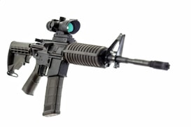 A black assault rifle with a tactical scope mounted on top and a pistol grip. The barrel is long and prominent, extending towards the viewer. The gun features a textured handguard and a magazine inserted into the magazine well.