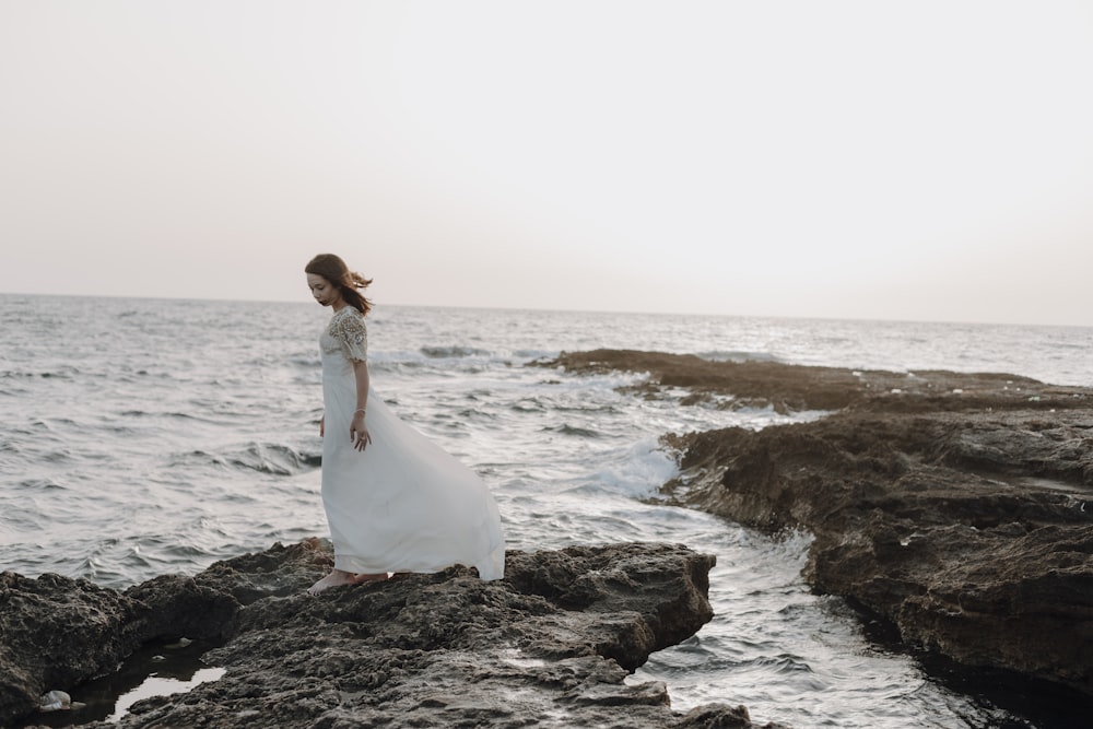 Eine Person in einem weißen Kleid steht an einem felsigen Strand