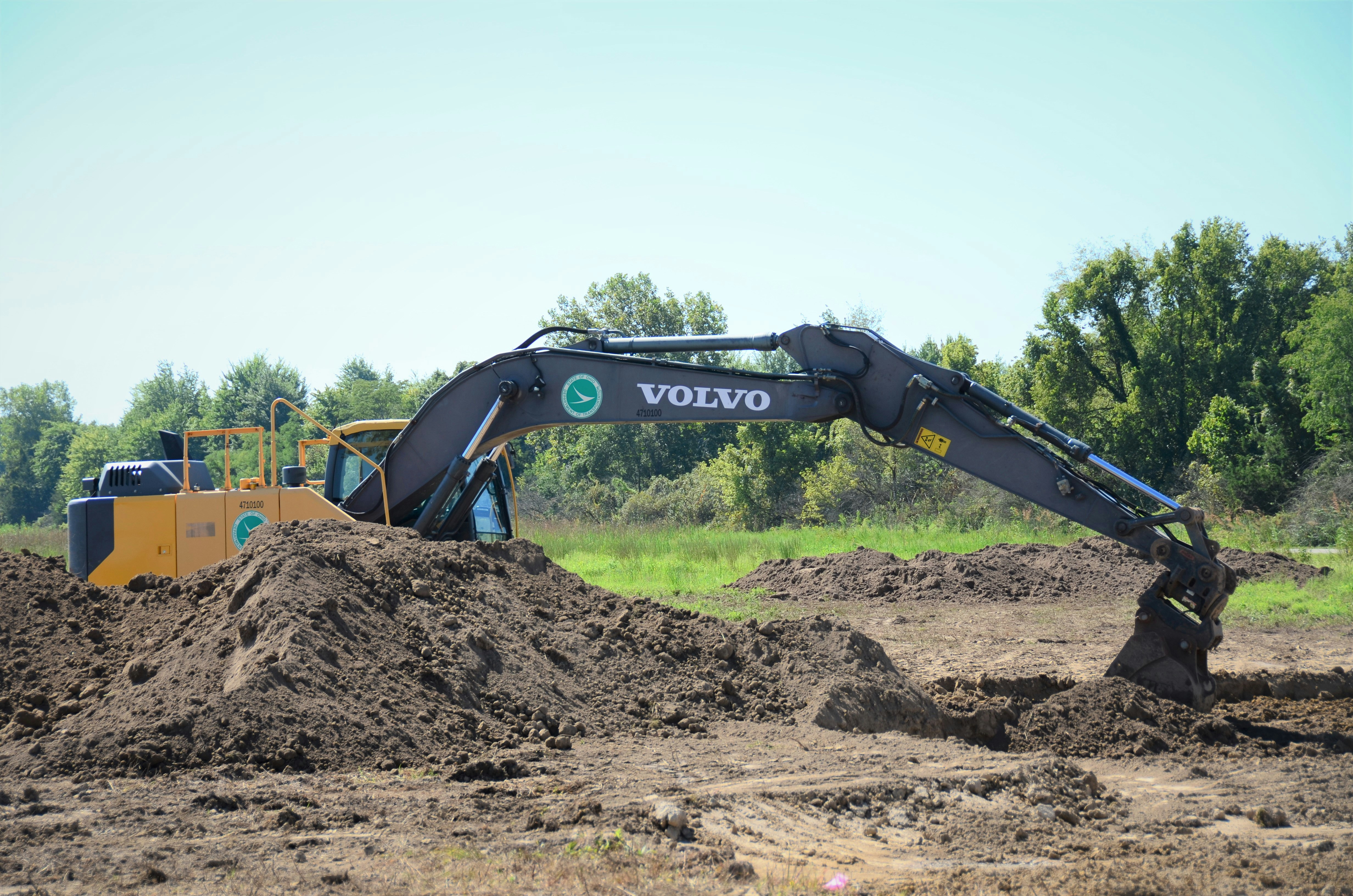 Excavator digging deep foundation trench on construction site, overcast sky, exposed earth walls