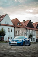A blue Ford Fiesta navigating a narrow European cobblestone street.