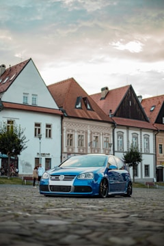 A blue Ford Fiesta navigating a narrow European cobblestone street.