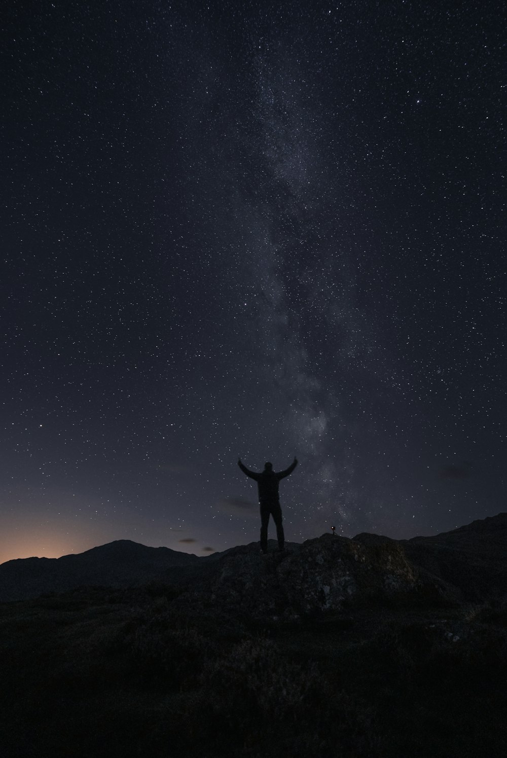 Una persona in piedi su una roccia con un cielo stellato sopra