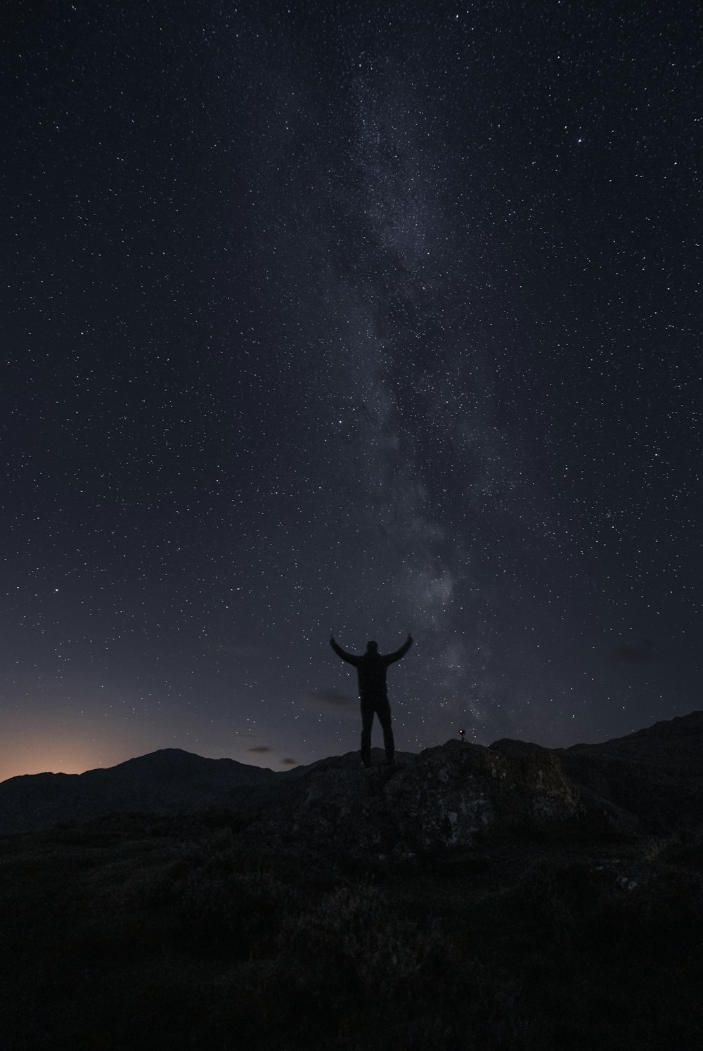 Eine Person, die auf einem Felsen mit einem Sternenhimmel darüber steht