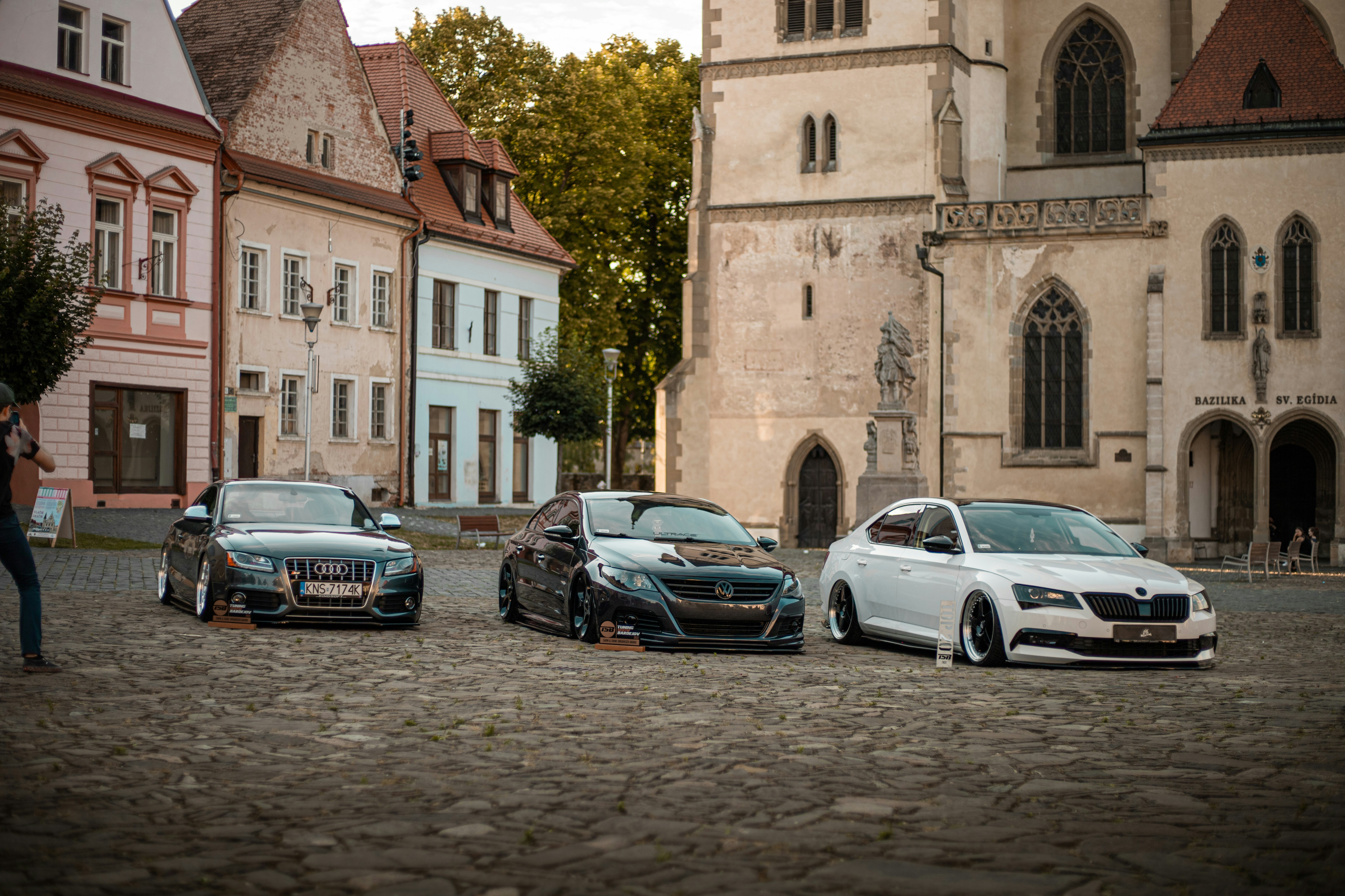 A group of cars parked in a cobblestone street photo – Free Car Image ...