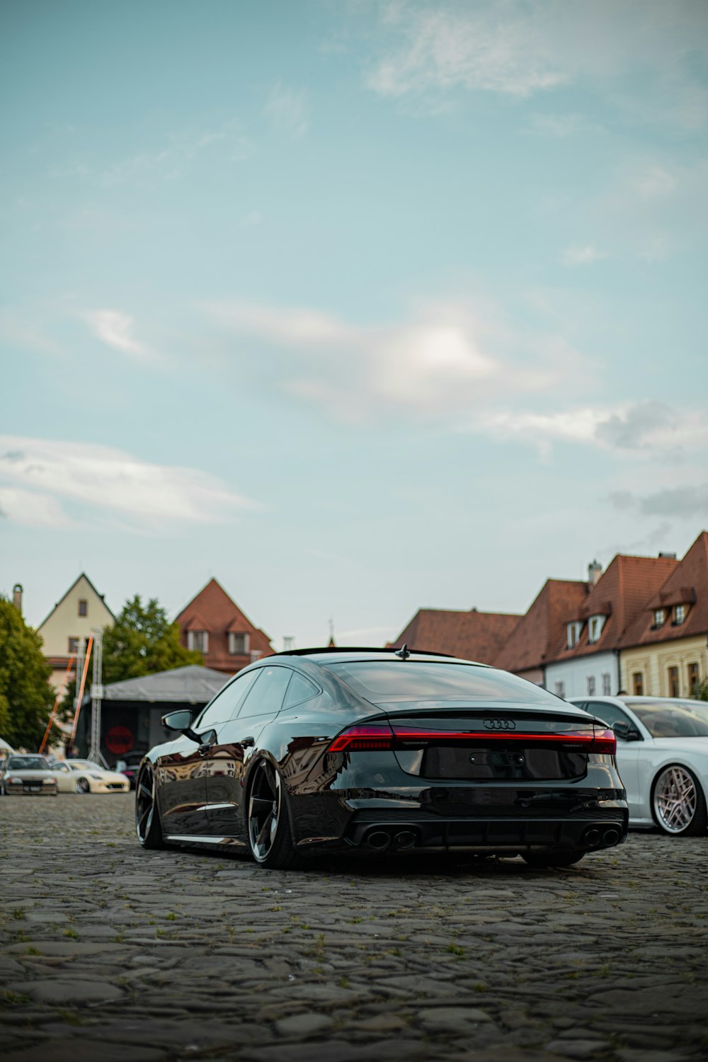 a black car parked in a parking lot with other cars and houses in the background