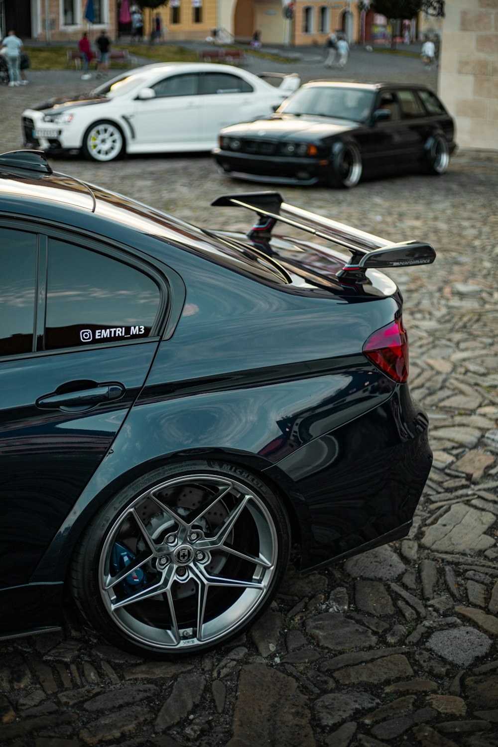 a black car parked on a brick road with other cars parked on the side