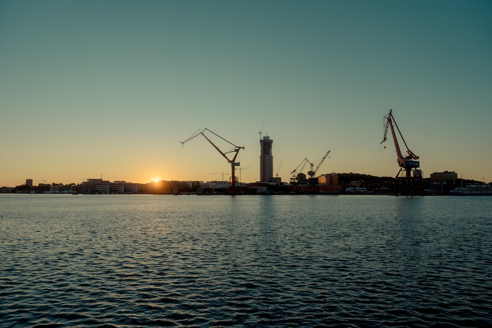 a body of water with cranes and buildings in the background