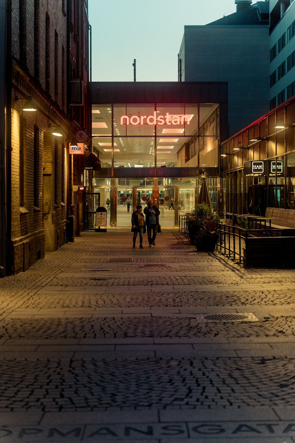 a couple of people walking on a brick road in front of a building